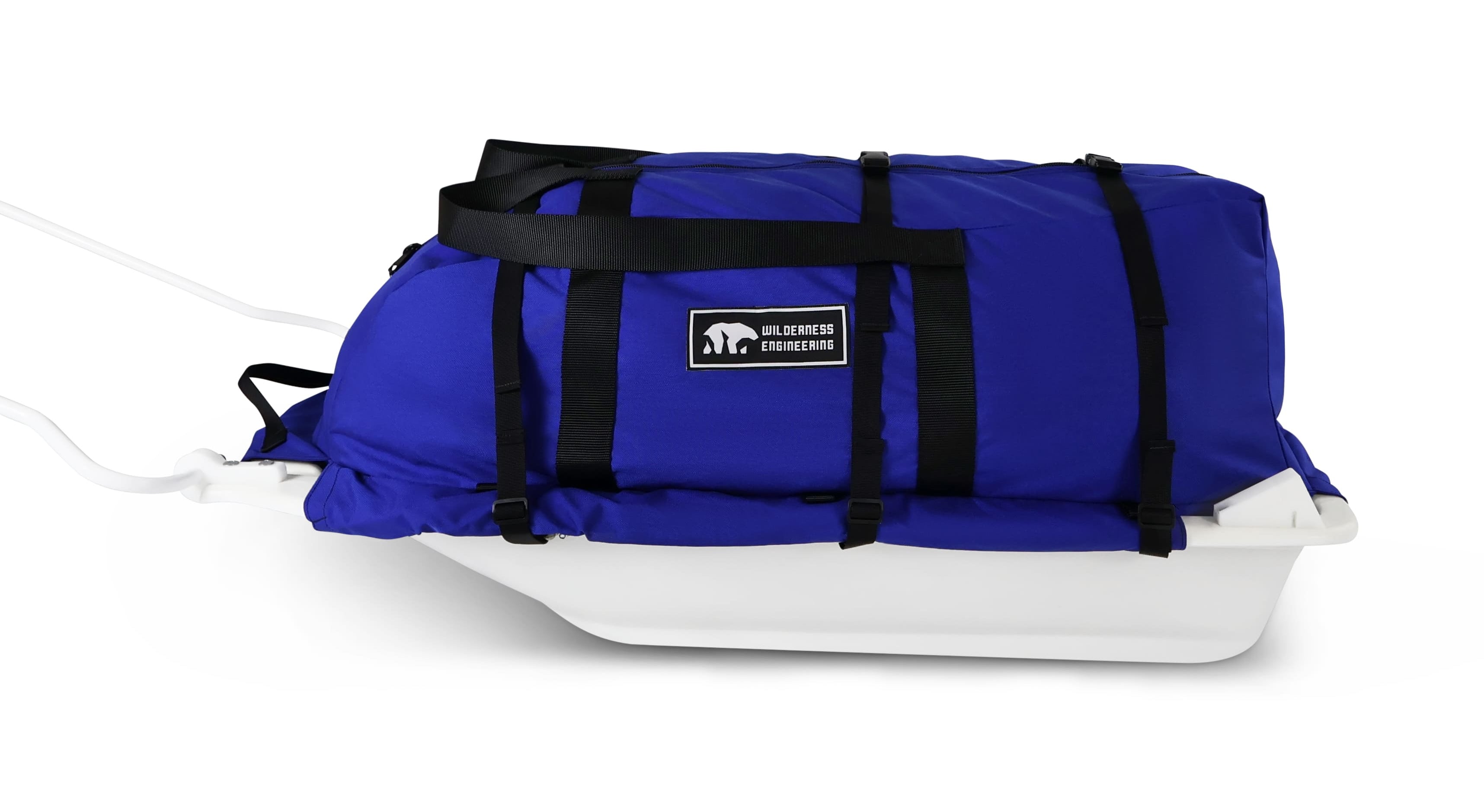 A Royal Blue snowmobile Sled Pulk cargo bag with black straps and a white plastic base, shown on a white studio background. With a tag labeled 'Wilderness Engineering'.