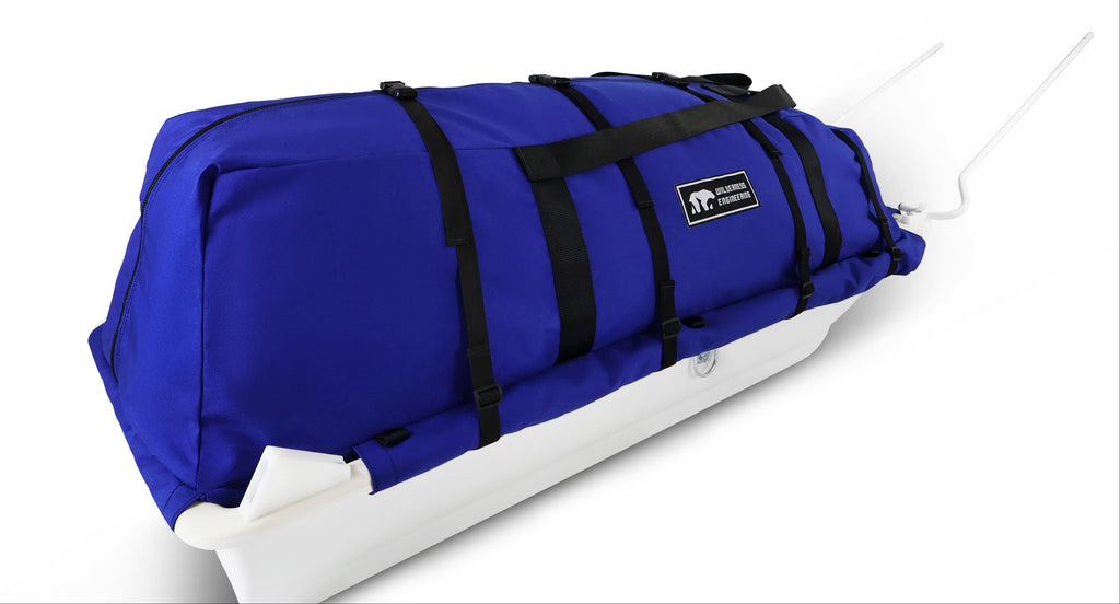 A blue snowmobile pulk sled cargo bag with black straps and a white plastic sled base, shown on a clean white background. A black label on the front displays the brand 'Wilderness Engineering'.