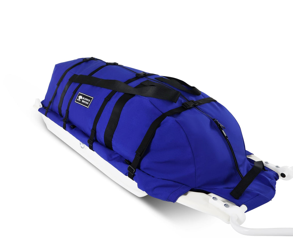 A Royal blue snowmobile Sled Pulk cargo bag with black straps and a white plastic base, shown on a white studio background. With a tag labeled 'Wilderness Engineering'.