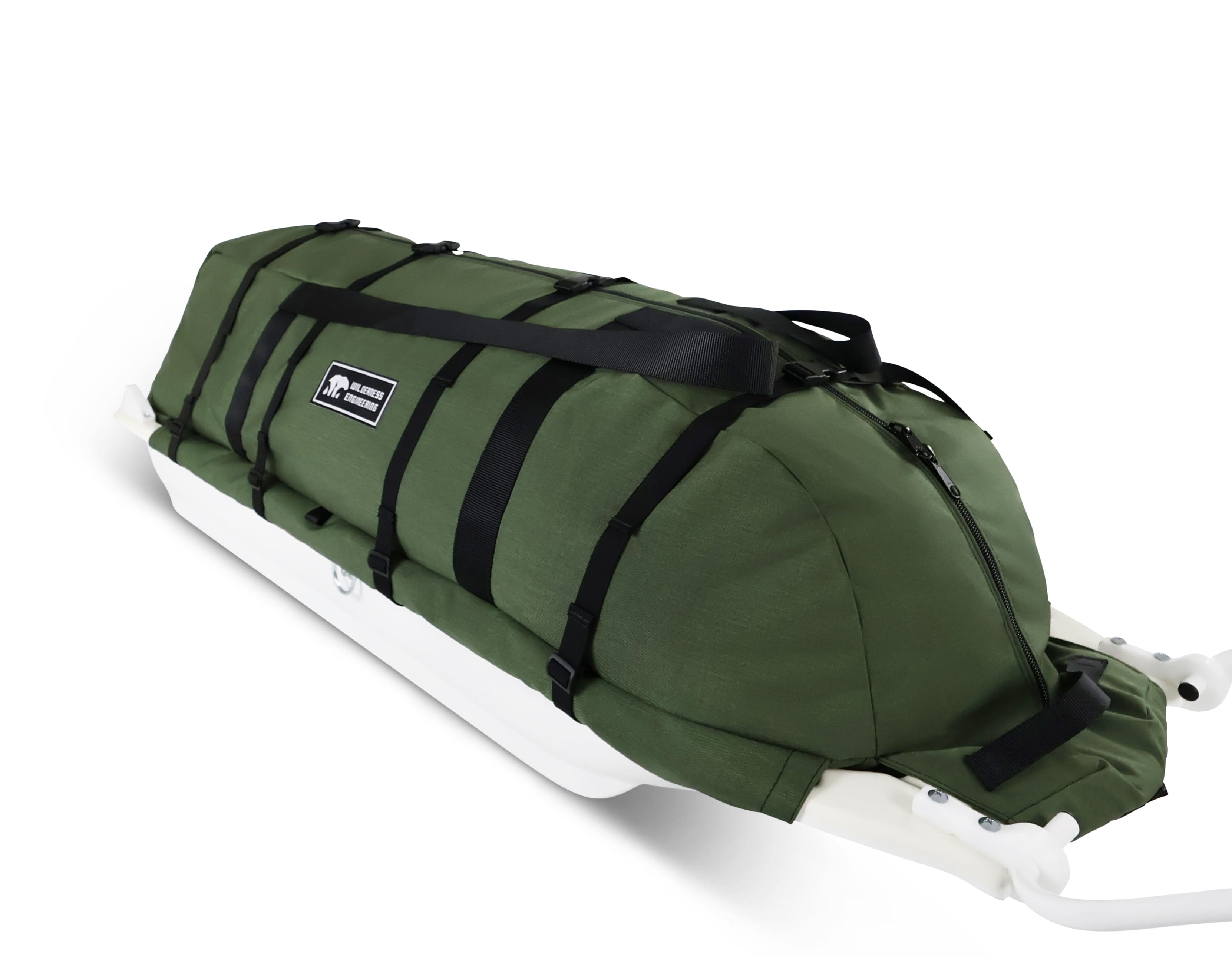 An olive green snowmobile cargo bag with black straps and a white plastic base, shown on a white studio background. With a tag labeled 'Wilderness Engineering'.